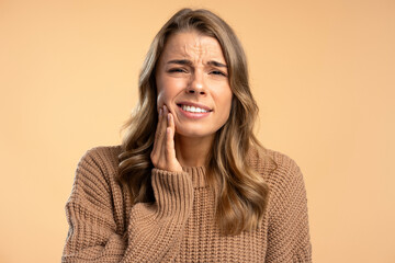 Portrait upset young woman touching face, toothache, looking at camera isolated on beige background