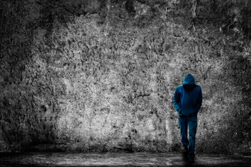 mysterious man in hood walking, in background is a concrete grunge wall