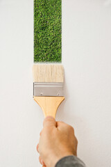 man hand with a brush painting a white wall with a strip of green grass