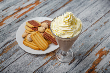 Chocolate milkshake with whipped cream on a wooden table. Milkshake and sweet cookies.