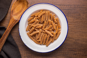 Raw whole grain fusilli pasta. Uncooked pasta on plate. Top view.
