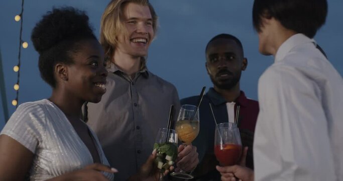 Group of people with cocktail glasses talking at outdoor party laughing socializing at night. Friendship and enjoyable celebration concept.