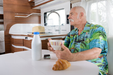 senior man taking breakfast inside camper van