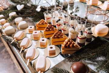 Fototapeta na wymiar A delicious wedding. White cake decorated with flowers. Candy bar for a banquet. Celebration concept. Fashionable desserts. Table with sweets, candies. Fruits