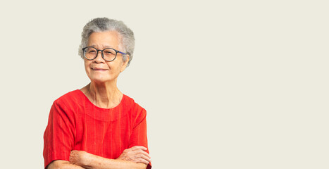 Beautiful senior woman with short white hair and glasses smiles at the camera while standing against a gray background.