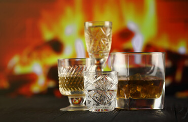 Different alcohol drinks in glass on wooden surface on fireplace background. Luxury elite alcohol in glass cups. Low key dark scene