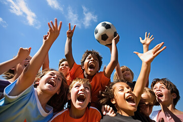 Group of joyful kids reaching for soccer ball under blue sky. Outdoor sports and teamwork.