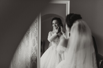 The bride in a wedding dress poses in her room, looking in the mirror. Black and white photo....