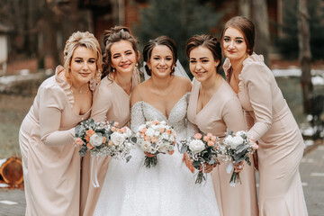 A brunette bride in a white elegant dress and her friends in gray dresses pose with bouquets....