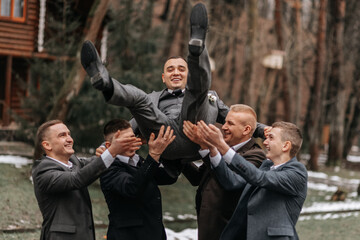 The groom and his friends are dressed in suits, fooling around in nature during a photo shoot. A group of men. Wedding in nature - Powered by Adobe