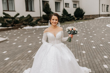 Fototapeta premium The bride in a white dress with a train and a long veil poses in nature, holding a bouquet. Walk. Winter wedding in nature.