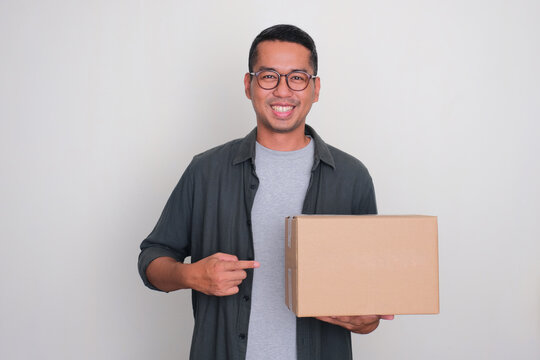 Adult Asian man smiling and pointing to a package box that he hold