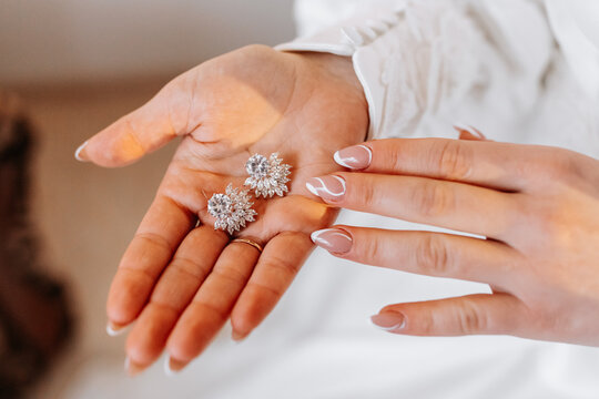 Cropped photo of the bride holding her earrings. Beautiful hands and manicure