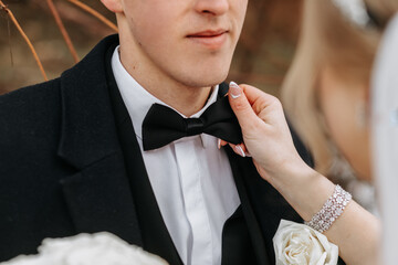 Cropped wedding portrait of the groom. The bride fixes the groom's bow tie. A man in a black suit....