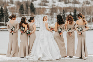 The bride and her bridesmaids pose, holding bouquets behind them, back view. Winter wedding - obrazy, fototapety, plakaty