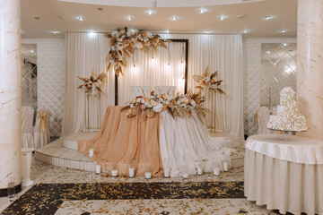 The wedding table of the bride and groom, decorated with flowers, dried ears of corn and white tulle, is made in nude color. Flowers on stands. Wedding details. light