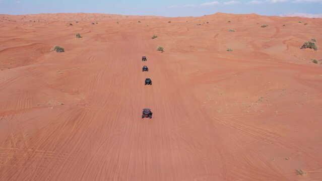 A drone flies over a caravan of buggies driving through the desert sand