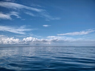 Tranquil scene of an ocean in pastel blue hues with white fluffy clouds in the sky