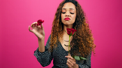 Beautiful young woman plays 'He loves me, he loves me not' game with red rose