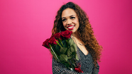 Beautiful multi-ethnic woman holds bunch of red roses, romance, pink studio - Powered by Adobe