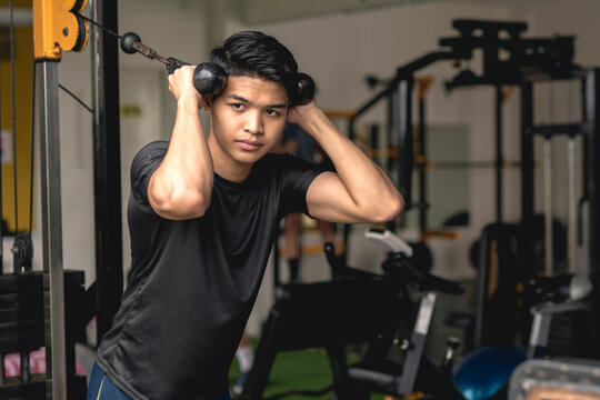 A young handsome asian man does standing rope crunches. Core exercises at the gym.