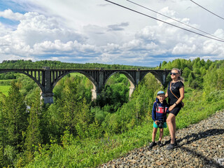 Railway bridge across the river in the south of the Kama region. A girl with a child on the background of the old viaduct of the Big Sars. The abandoned Oktyabrsky viaduct in the Perm Region. Russia.