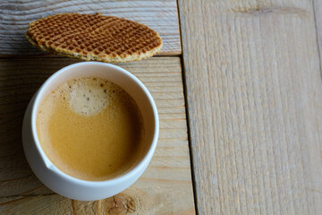 One cup of black coffee with a stroopwafel on the wooden background. A cup of coffee on the wooden table with a biscuit