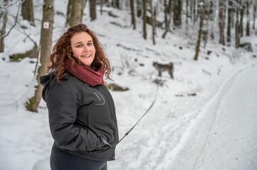 Young woman enjoying the winter season, standing in a snow covered forest with a smile on her face