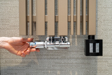 Woman hand adjusting temperature with thermostat on modern radiator