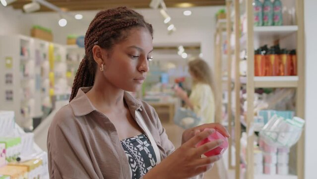 Medium shot of female customer taking cream from shelf at cosmetic department during shopping
