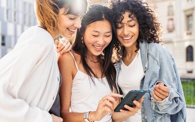 Multiracial young women using smart mobile phone device outside - Happy female friends watching funny video on smartphone - Trendy technology life style concept