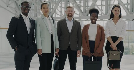 Portrait of diverse group of businesspeople standing in airport lobby smiling looking at camera. Teamwork and commuting business concept.