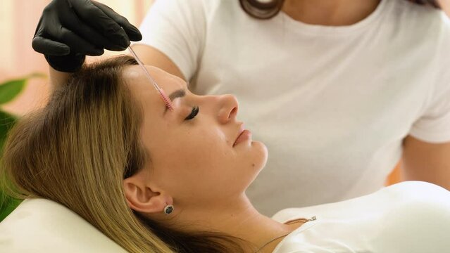 Beauty master brushing client's brows after permanent makeup procedure. Closeup shot