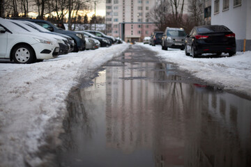 Puddle in the parking lot. Melting snow on the street. Parking in winter at the houses.