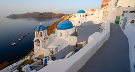 street of traditional greek village Oia of Santorini, with blue domes against Aegan sea and...