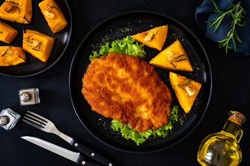 Crispy breaded seared chicken cutlet with baked pumpkin  on wooden table
