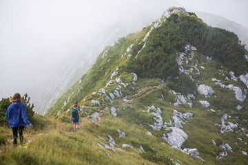 Fototapeta premium People trekking up a steep incline towards a range of misty mountains in Triglav National Park