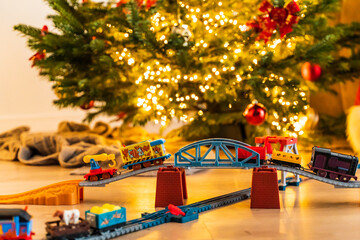 A toy steam locomotive on the floor under a decorated Christmas tree against the background of a garland of bokeh lights. Christmas and new year celebration concept, background. free space