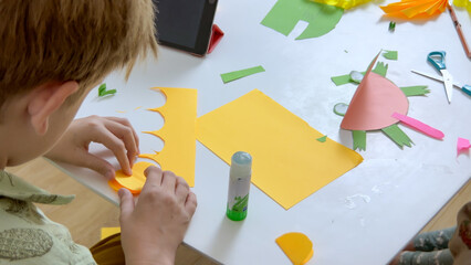 Kid creating an applique with colored paper and glue. Concept of hobby