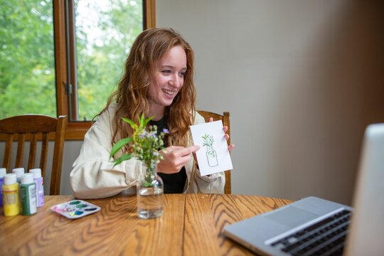 Young art teacher holding a drawing and explaining the lesson to her students during an online class
