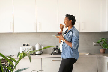 Smiling pregnant woman eating red grapes in kitchen