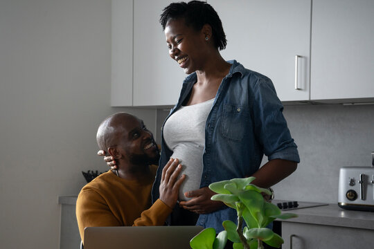 Smiling man touching pregnant woman's belly in kitchen