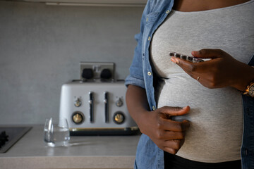 Mid section of pregnant woman holding capsules - obrazy, fototapety, plakaty