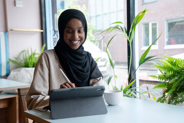 Young woman in hijab working on tablet in cafe