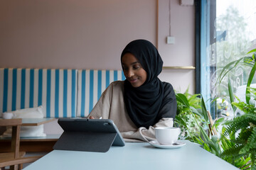 Young woman in hijab working on tablet in cafe