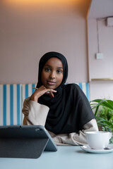 Portrait of young woman in hijab working on tablet in cafe
