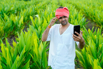Young indian farmer showing debit or credit card at his green agriculture field, using mobile phone