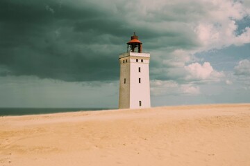 there is a small lighthouse on the beach under a stormy sky