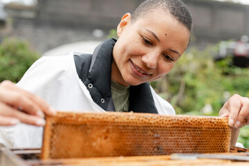 Smiling female beekeeper removing frame from beehive in urban garden