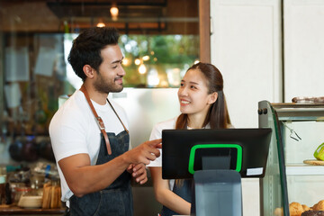 A business couple owns a cafe. Young Asian woman with multiethnic men. Looking  the cash register month's sales have  lot set. Both of  had happy smiles on their faces, looking at each other happily.